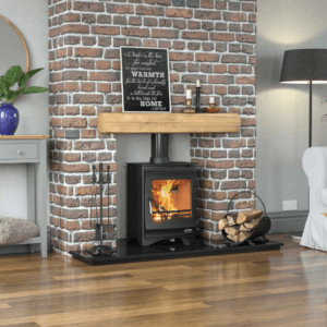 Stunning black stove with fire lit behind large viewing window and matching blaack pipe work. Set on a black granite hearth with rustic timber mantle and brick feature wall