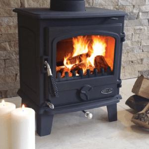 The Eden compact multi fuel Stove. Its superb cast iron construction and traditional design is pictured here in black with a black and silver handle. A burning fire blazes in the viewing window as the stove sits against a grey cladding wall.