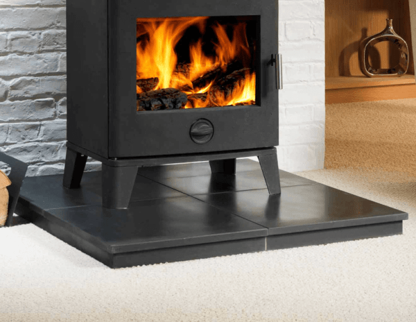 Black Granite Stove Hearth Filled, pictured with a black stove perched on top, fire burning inside the stove, grey clad backdrop